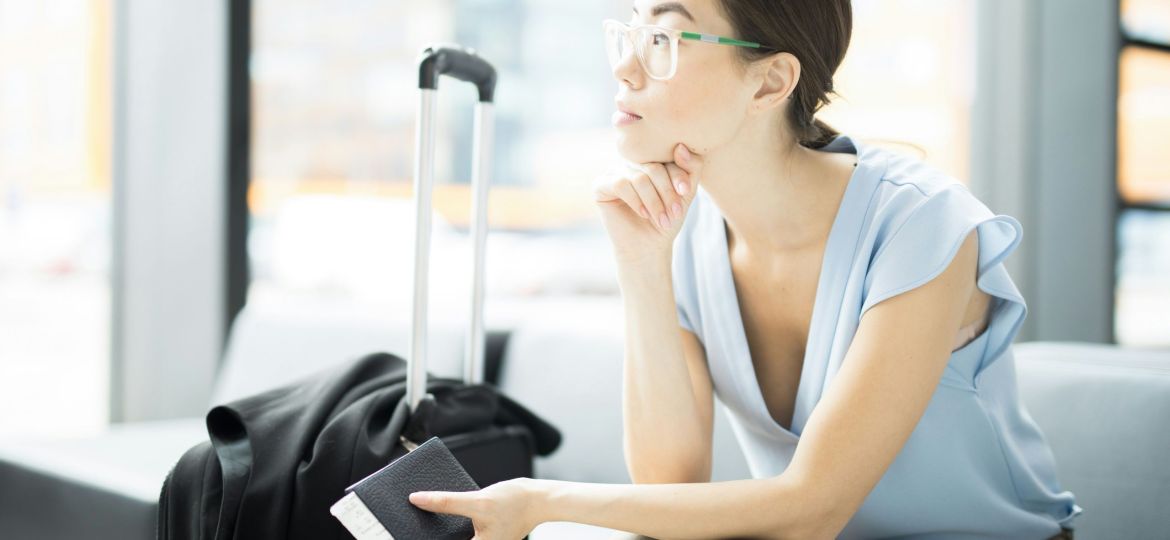 A woman sitting in an airport waiting area with her luggage, holding a passport and boarding pass
