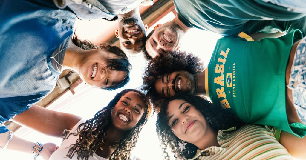 A diverse group of smiling friends standing in a huddle, looking down at the camera from a low angle
