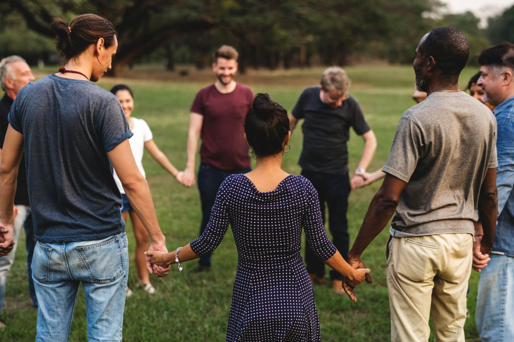 A group of people standing in a grassy field, holding hands in a circle
